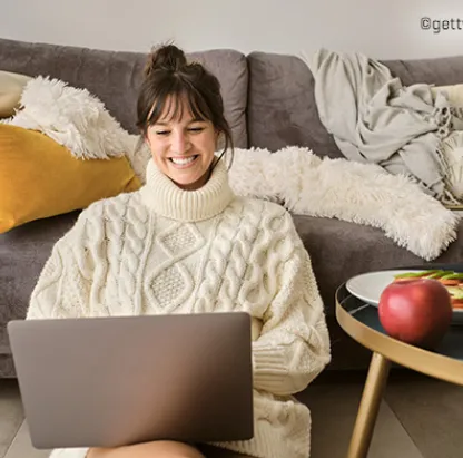 Femme dans un salon, devant un canapé, sur le sol, tapant sur un ordinateur portable.